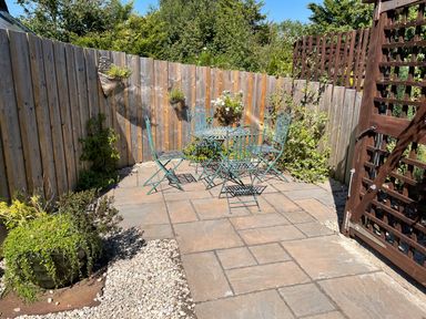 A small outdoor patio with a metal table and four chairs surrounded by a wooden fence and plants at Stable Cottage in Shipham