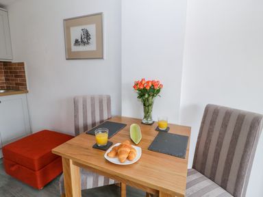 A dining table with two glasses of orange juice croissants and a vase of flowers with chairs at Bwlch Y Gwynt Bach in Llangefni