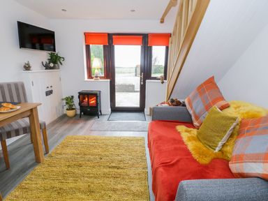A living room with a grey sofa covered with cushions and a throw beside a wooden staircase at Bwlch Y Gwynt Bach in Llangefni