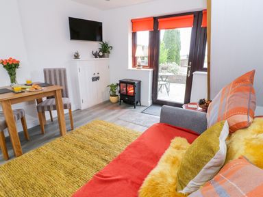 A living room with a sofa yellow pillow and a wooden table with two chairs at Bwlch Y Gwynt Bach in Llangefni