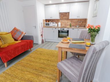 A kitchen and dining area with a small table set for two and a sofa with cushions at Bwlch Y Gwynt Bach in Llangefni