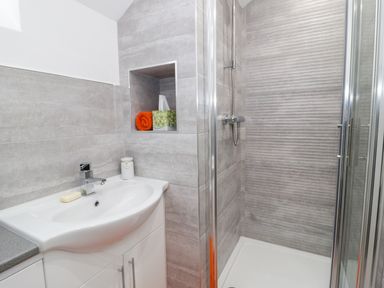A bathroom with a sink, soap, tissue box, towel, and a shower cubicle at Bwlch Y Gwynt Bach in Llangefni