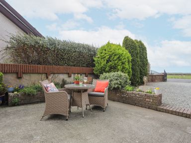 A patio with two wicker chairs and a round table with plants and glasses in a garden at Bwlch Y Gwynt Bach in Llangefni