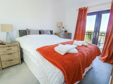 A bedroom with a bed covered in white and orange bedding and towels on top with bedside tables and lamps and orange curtains at Bwlch Y Gwynt Bach in Llangefni