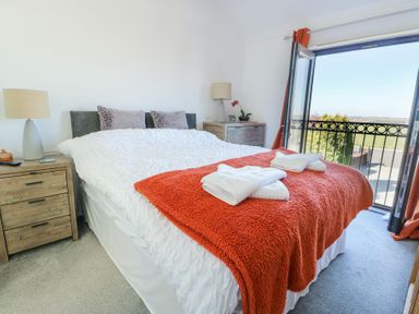 A bedroom with a double bed and orange blanket with two bedside tables and open door to balcony at Bwlch Y Gwynt Bach in Llangefni