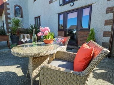 An outdoor patio area with wicker chairs a table with a bottle two wine glasses and a potted plant at Bwlch Y Gwynt Bach in Llangefni