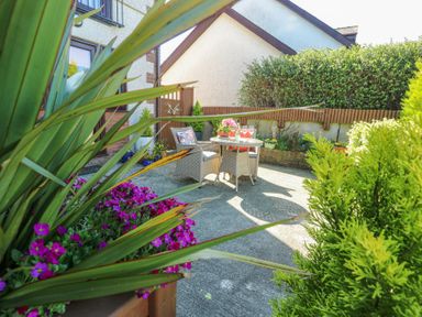A patio with two chairs and a round table with drinks and flowers surrounded by plants Bwlch Y Gwynt Bach Llangefni