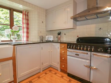 A kitchen with a stove oven toaster and a window with flowers on the windowsill at Ribby Farmhouse in Lerryn