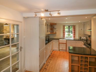 A kitchen with wooden floors white cabinets a black countertop and a window with red checked curtains at Ribby Farmhouse in Lerryn