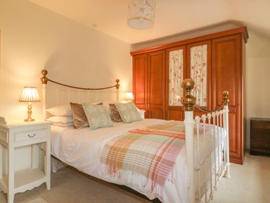 A bedroom with a white metal bed frame with brass accents bedside tables with lamps and a wooden wardrobe with floral curtains at Ribby Farmhouse in Lerryn