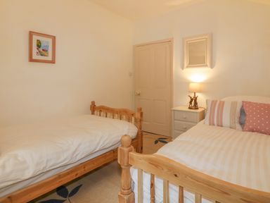 A bedroom with two wooden single beds a nightstand with a lamp and cushions on one bed at Ribby Farmhouse in Lerryn