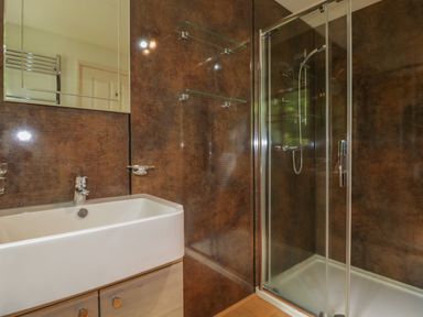 A bathroom with a white sink and wooden cabinet next to a glass shower enclosure at Ribby Farmhouse in Lerryn