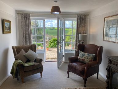 A sitting room with two armchairs and a door leading to a garden at Ribby Farmhouse in Lerryn