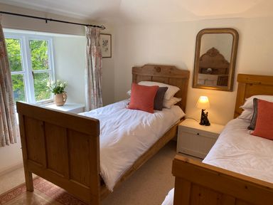 A bedroom with two wooden single beds a nightstand with a lamp and a mirror on the wall at Ribby Farmhouse in Lerryn