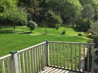 A wooden balcony overlooking a garden with grass trees and a stone path at Ribby Farmhouse in Lerryn