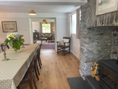 A dining room with a polka dot tablecloth on the table and a stone fireplace with wood logs at Ribby Farmhouse in Lerryn