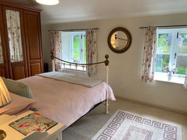 A bedroom with a bed covered with pink bedding and floral curtains on windows at Ribby Farmhouse in Lerryn
