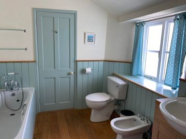 A bathroom with a bathtub toilet bidet sink and window with curtains at Ribby Farmhouse in Lerryn