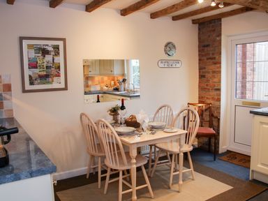 A dining area with a wooden table and four chairs set for a meal next to a door and a brick wall at Cream Door Cottage in Kidderminster
