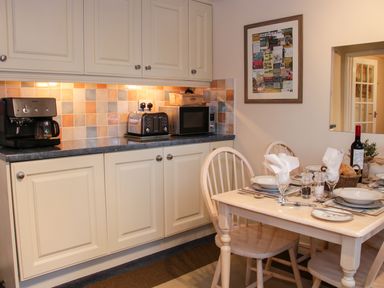 A kitchen with a coffee maker, toaster, microwave, and a dining table set for four at Cream Door Cottage in Kidderminster