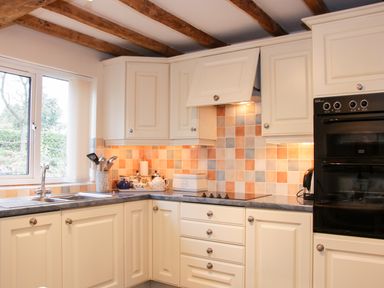 A kitchen with white cabinets black oven tiled backsplash and a window at Cream Door Cottage in Kidderminster