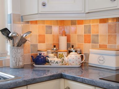 A kitchen corner with utensils in a holder teapots on a tray a paper towel holder and a bread box at Cream Door Cottage in Kidderminster
