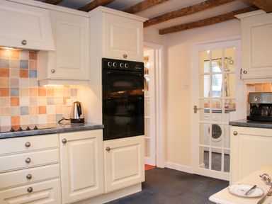 A kitchen with white cabinets black oven and glass door leading to a laundry room at Cream Door Cottage Kidderminster