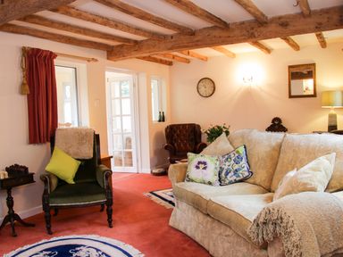 A living room with a beige sofa and floral cushions a green armchair and wooden ceiling beams at Cream Door Cottage in Kidderminster