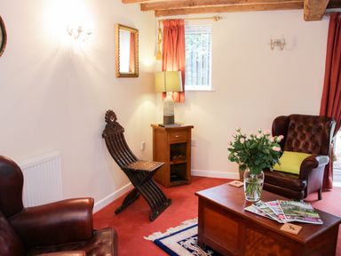 A sitting room with leather armchairs a wooden coffee table with magazines and flowers and a wooden cabinet with a lamp at Cream Door Cottage in Kidderminster