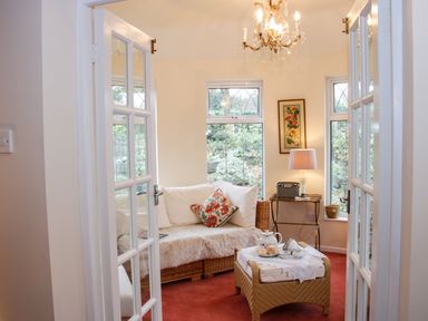 A small sitting room with wicker furniture a tea set on a table and windows showing a garden view at Cream Door Cottage in Kidderminster