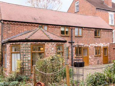 A brick house with multiple wooden framed windows and doors with a tiled roof and garden area in front at Cream Door Cottage in Kidderminster
