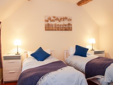 A bedroom with two single beds blue pillows and white bedside tables with lamps at Cream Door Cottage in Kidderminster