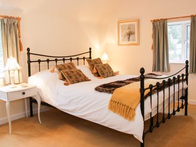A bedroom with a black metal bed frame bedside tables with lamps and windows with curtains at Cream Door Cottage in Kidderminster