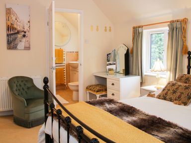 A bedroom with a bed a green armchair a dressing table with a stool and an open door leading to a bathroom at Cream Door Cottage in Kidderminster