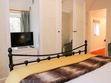 A bedroom with a black metal bed frame a yellow blanket and a faux fur throw a white dresser with a television and a remote a mirrored wardrobe and an open door at Cream Door Cottage in Kidderminster