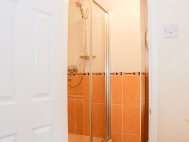 A shower area with orange and white tiles and a glass door at Cream Door Cottage in Kidderminster