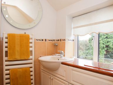 A bathroom sink with a round mirror above and yellow towels on a white towel rack next to a window with a roller blind at Cream Door Cottage in Kidderminster
