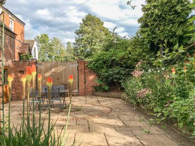 An outdoor patio with stone paving a metal table and chairs plants and flowers around the edges at Cream Door Cottage in Kidderminster