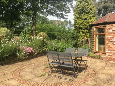 An outdoor patio area with a metal table and four chairs surrounded by plants and flowers at Cream Door Cottage in Kidderminster