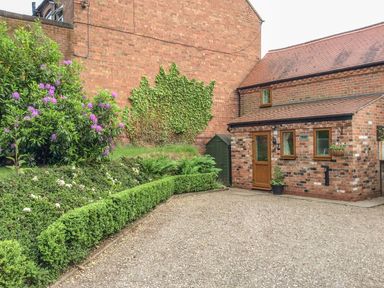 A brick cottage with a wooden door and windows next to a garden with hedges and flowering plants at Cream Door Cottage in Kidderminster