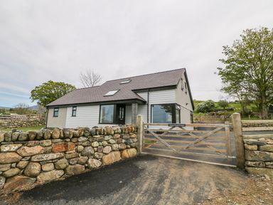 A house behind a wooden gate with stone walls and trees around at Llwyd Coed Canol in Llanllyfni near Penygroes