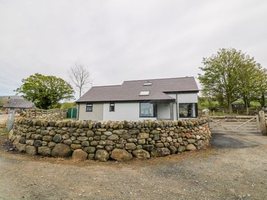 A house with a stone wall and wooden gate surrounded by trees at Llwyd Coed Canol in Llanllyfni near Penygroes