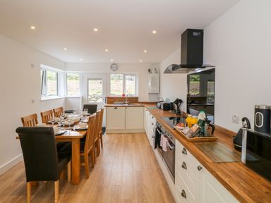 A kitchen with a wooden dining table set with dishes and glasses alongside a countertop with appliances at Llwyd Coed Canol in Llanllyfni near Penygroes