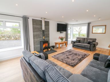 A living room with two sofas a wood burning stove a wall mounted tv and large windows at Llwyd Coed Canol in Llanllyfni near Penygroes