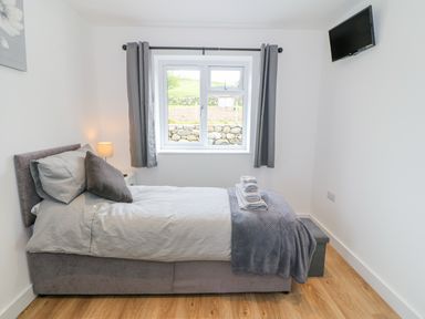 A bedroom with a single bed with pillows and folded towels next to a window with gray curtains at Llwyd Coed Canol in Llanllyfni near Penygroes