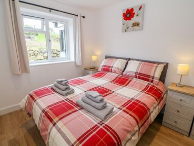 A bedroom with a double bed with red plaid bedding two bedside tables with lamps and a window at Llwyd Coed Canol in Llanllyfni near Penygroes