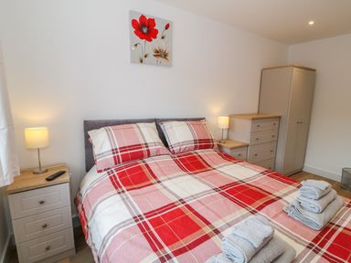 A bedroom with a bed with red plaid bedding a wardrobe two bedside tables with lamps and folded towels on the bed at Llwyd Coed Canol in Llanllyfni near Penygroes