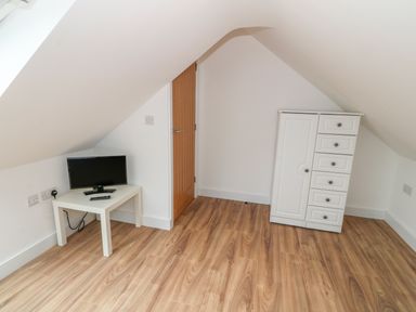 A small attic room with wooden floor a white table with a TV and a remote and a white cabinet with drawers at Llwyd Coed Canol Llanllyfni near Penygroes