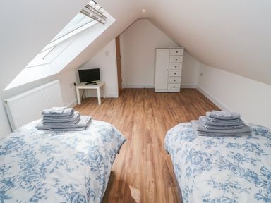 A bedroom with two single beds with floral bedding, a small white table with a television, a white chest of drawers and a skylight window at Llwyd Coed Canol in Llanllyfni near Penygroes