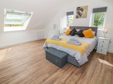 A bedroom with a bed with pillows and blankets a chest at the foot of the bed two bedside tables with lamps a dresser with a mirror and two windows at Llwyd Coed Canol in Llanllyfni near Penygroes